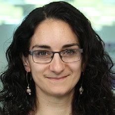 Headshot of a woman with dark, curly hair and glasses, smiling.