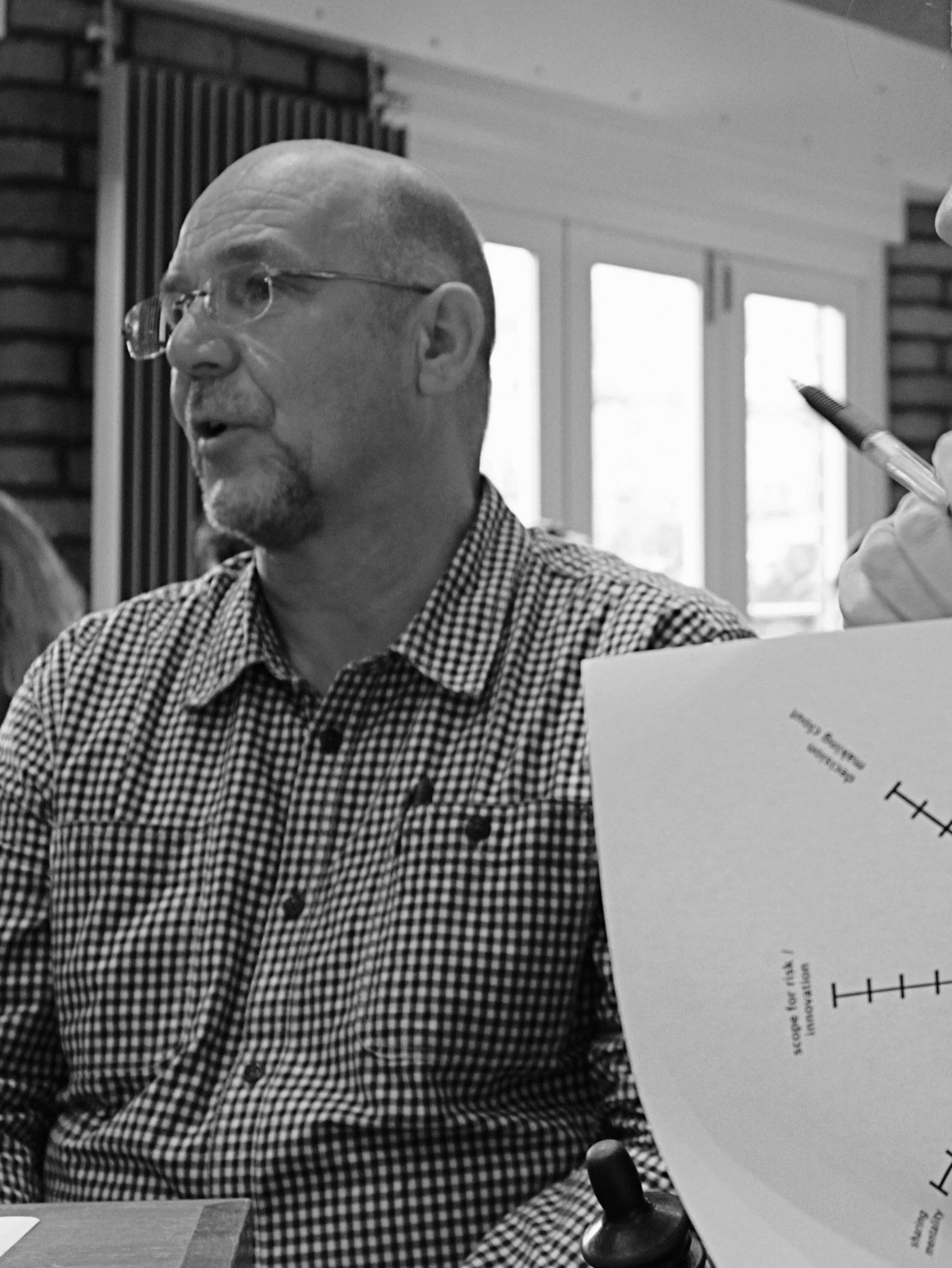 Man in a plaid shirt speaking during a meeting, with a visible chart displaying axes for decision making and risk innovation in the foreground.