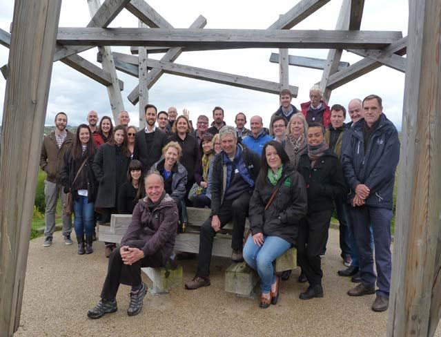 Group photo of diverse people posing outdoors under a large wooden architectural structure.