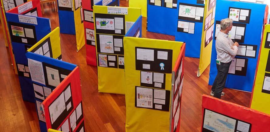 A man views student projects displayed on colorful presentation boards at an exhibition.