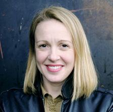 Headshot of a smiling woman with blonde hair, wearing a dark jacket.