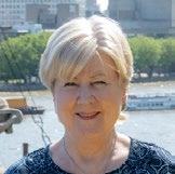 Headshot of a smiling woman with blonde hair against a city waterfront background.