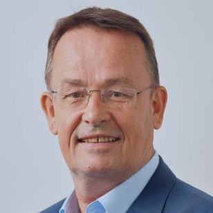 Headshot of a smiling man with short brown hair and glasses, wearing a blue shirt and jacket.