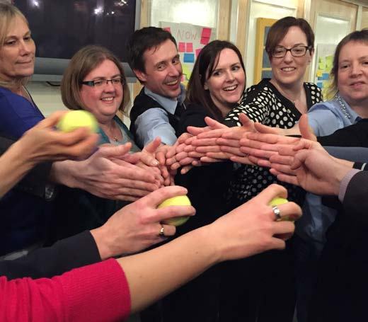 Group of adults engaged in a team-building exercise, holding and passing small yellow balls, showing interaction and collaboration.