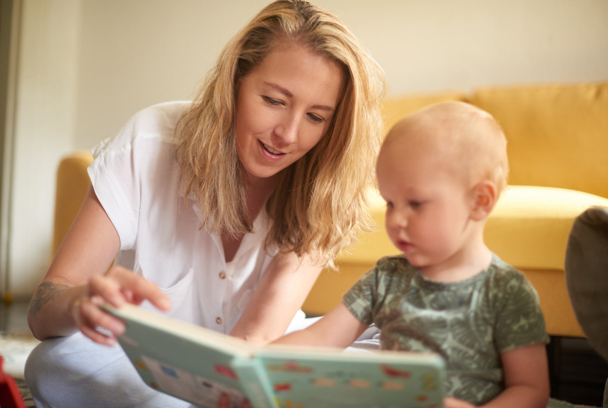 A woman with blonde hair reads a book to a young child with fair hair in a cozy indoor setting.