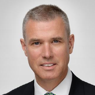 Headshot of a smiling man with short grey hair, wearing a suit and patterned tie.