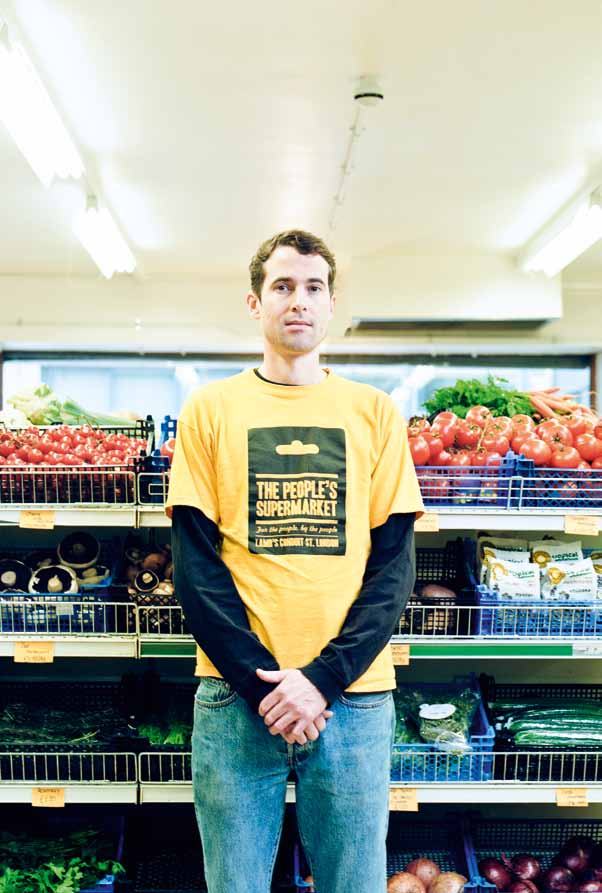 Man in a "The People's Supermarket" t-shirt stands in front of a supermarket produce section.
