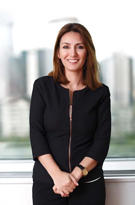 Smiling woman in a black jacket and pants, with a city skyline blurred in the background.