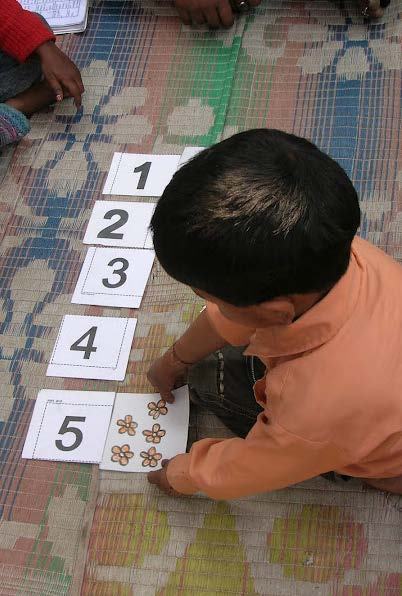 A child on a mat matches number cards 1-5 with cards showing corresponding quantities of flowers, demonstrating a learning activity.