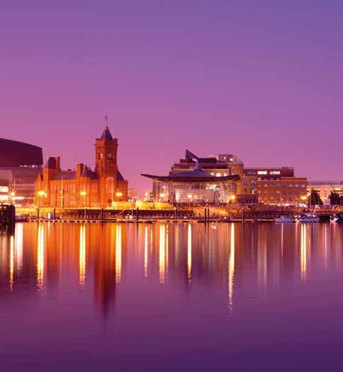 Cardiff Bay waterfront at dusk, with illuminated buildings reflected in the purple-hued water.