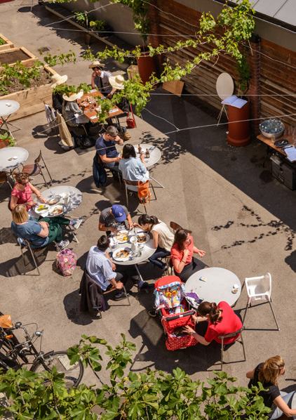 Overhead view of a busy outdoor restaurant patio with several groups of people dining at round tables on a sunny day.