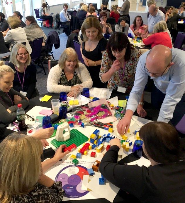 A group of people actively participating in a workshop, building with colorful LEGO blocks and other items around a table.