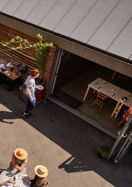 Overhead view of a restaurant's outdoor patio entrance, with a server carrying a plate of food towards the seating area.