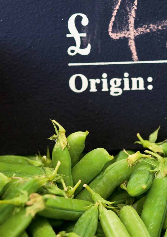 Fresh green peas in a pile with a chalkboard sign displaying a price (pounds) and the word "Origin:".