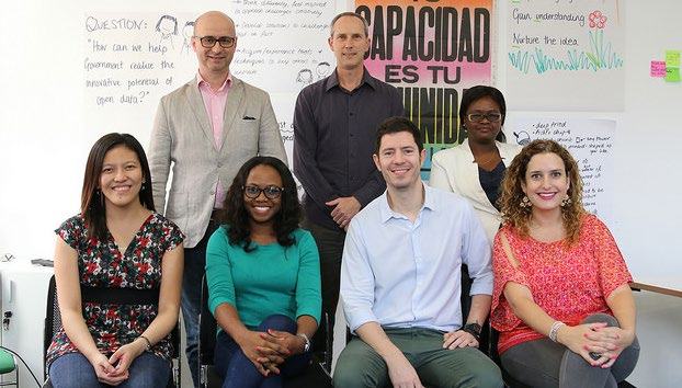 Group photo of eight people in a workshop setting, with a whiteboard asking "How can we help the government reduce the innovative potential of open data?"