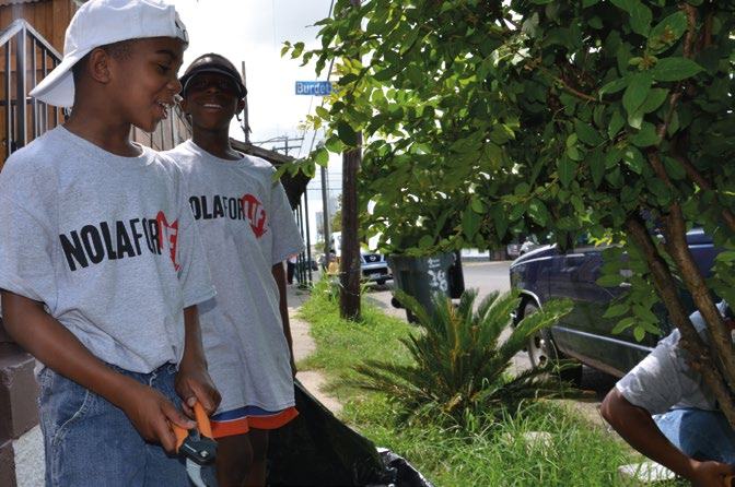Two boys in "NOLA FOR LIFE" shirts participate in an outdoor community service activity, trimming a tree.
