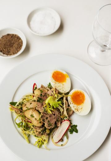 A plate featuring a salad with tuna, white beans, radish, and two halved soft-boiled eggs, with salt and pepper bowls.