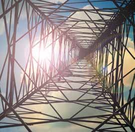 Upward view inside a metal lattice structure, likely a transmission tower, with bright sunlight shining through.