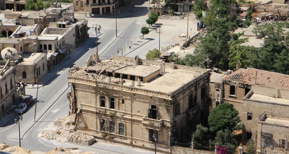 Aerial view of a town with heavily damaged and partially collapsed buildings, indicative of conflict or disaster aftermath.