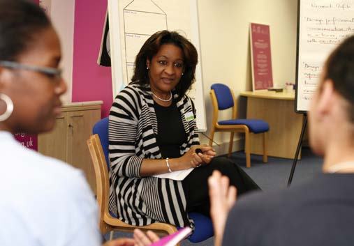 A woman in a striped cardigan sits attentively in a group discussion or training session, with a whiteboard visible in the background.