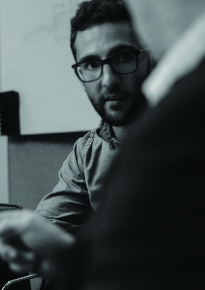 Black and white photo of a man with glasses and a beard, looking attentive.