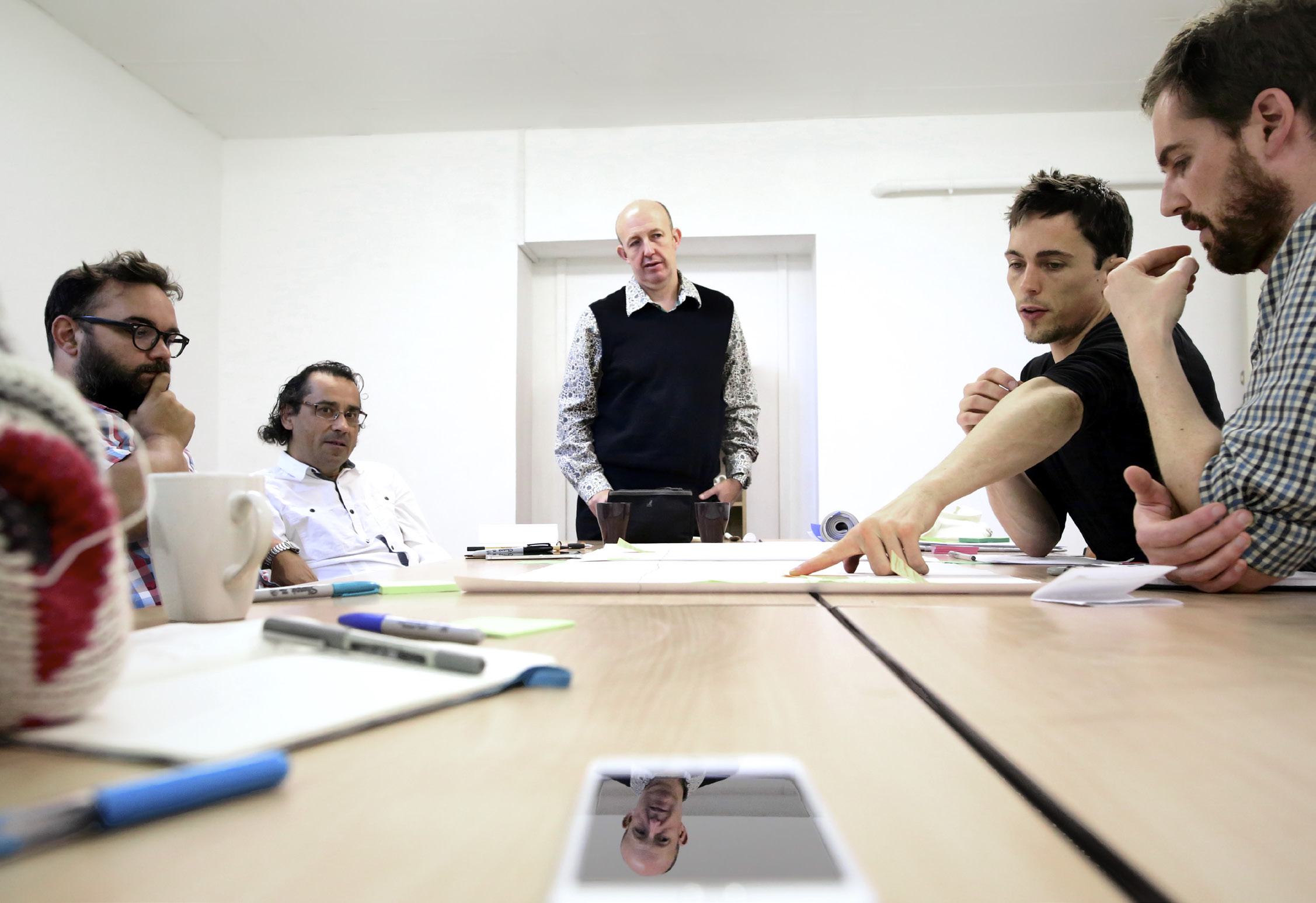 A team of diverse professionals collaborating around a table in a meeting, discussing ideas and pointing to documents.
