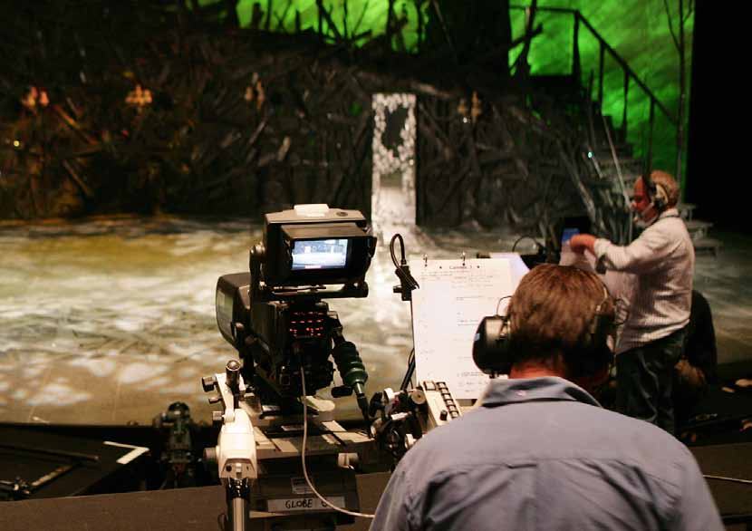 Camera operator with headphones stands beside a camera on tracks, ready to film a stage set with golden props.