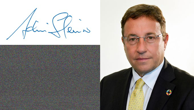 Blue signature next to a headshot of a man in a suit and glasses wearing a colorful lapel pin