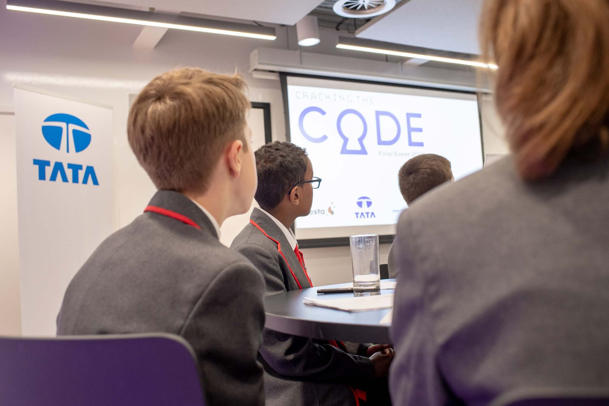 Students in school uniforms attending a "CRACKING THE CODE Final Event" with TATA branding displayed on a screen and banner.