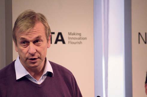 Man in a purple sweater speaking, with a "NESTA Making Innovation Flourish" logo partially visible in the blurred background.