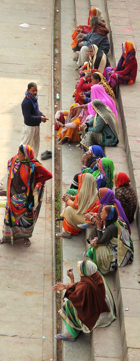 A group of people, mostly women in colorful saris, sitting on stone steps while a man stands and speaks to one.