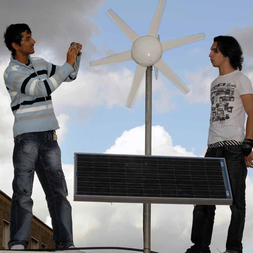 Two men inspecting a small wind turbine and solar panel setup on a rooftop, one taking a photo.
