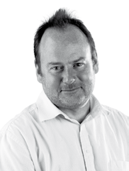 Black and white headshot of a man with short, spiky hair and a beard, wearing a collared shirt, looking forward and slightly smiling.