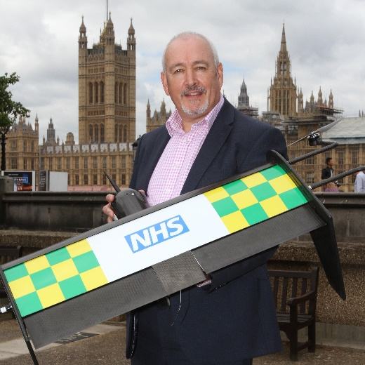 Man holding a drone marked with 'NHS' in front of the Houses of Parliament, showcasing a specific application of drone technology.