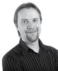 Black and white headshot of a man with longish hair and a goatee, wearing a striped shirt, looking forward and smiling.