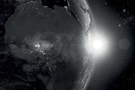 Grayscale image of Earth from space at dawn, showing clouds, city lights, and a bright sunburst on the horizon over Africa and the Middle East.