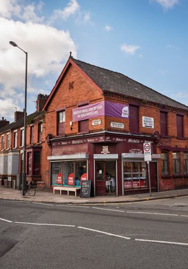 Exterior view of Mitchells Bakery on a street corner, a brick building with a purple banner.