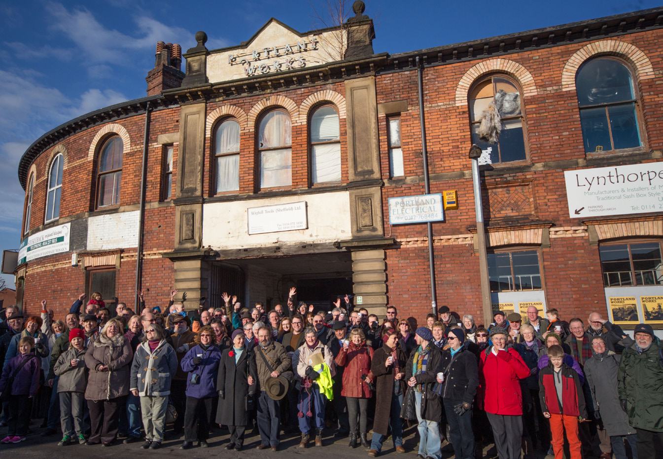A large group of people waving in front of the historic brick building known as Portland Works.
