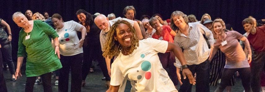 Diverse group of people participating in a group exercise or workshop, smiling and performing a coordinated movement.
