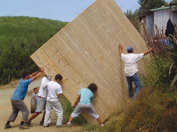 Several men in casual clothes collaboratively pushing a large wooden panel up a dirt path in a rural setting.