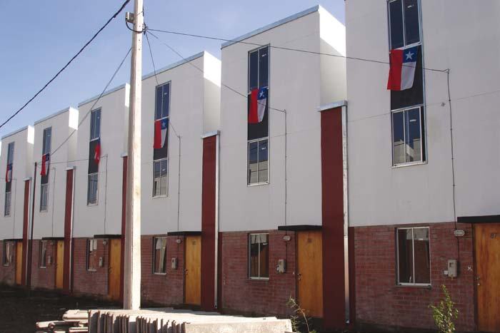 A row of recently constructed multi-story white houses with brick bases, each displaying a Chilean flag from an upper window.