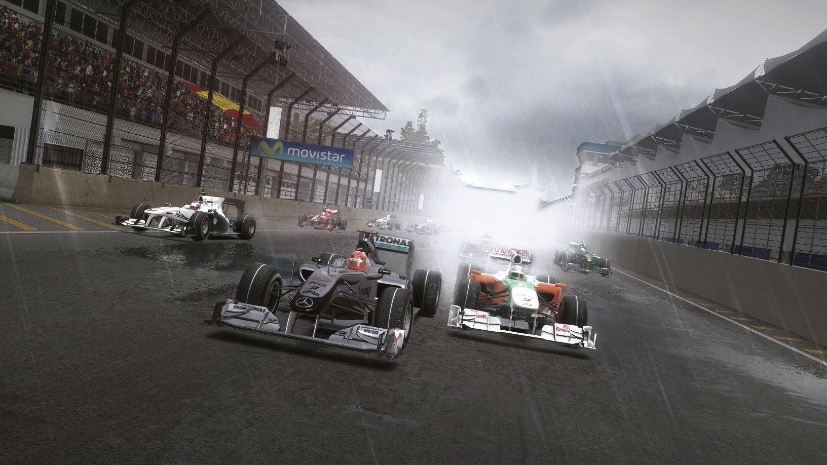 Screenshot from a racing video game depicting multiple Formula 1 cars speeding on a wet track in the rain, with spectators in grandstands.