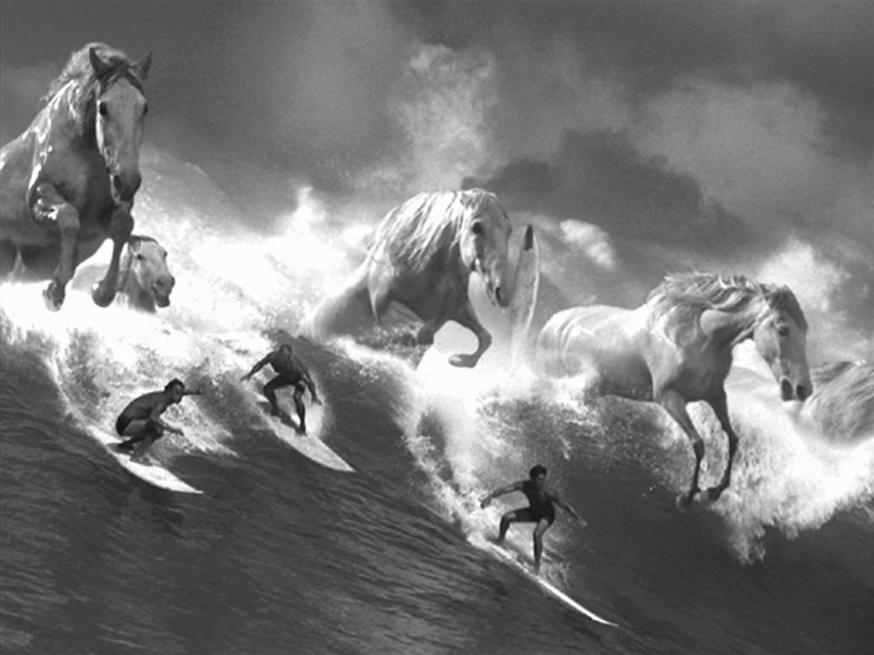 Black and white image of surfers riding large waves, with ethereal galloping horses superimposed on the water, creating a surreal scene.