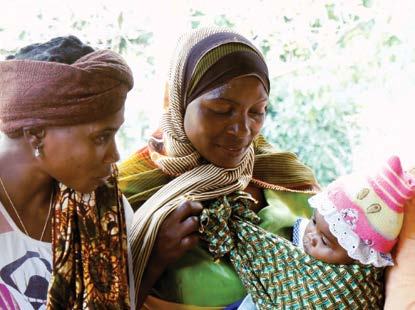 Two women looking at a baby wrapped in a patterned blanket and wearing a striped hat.