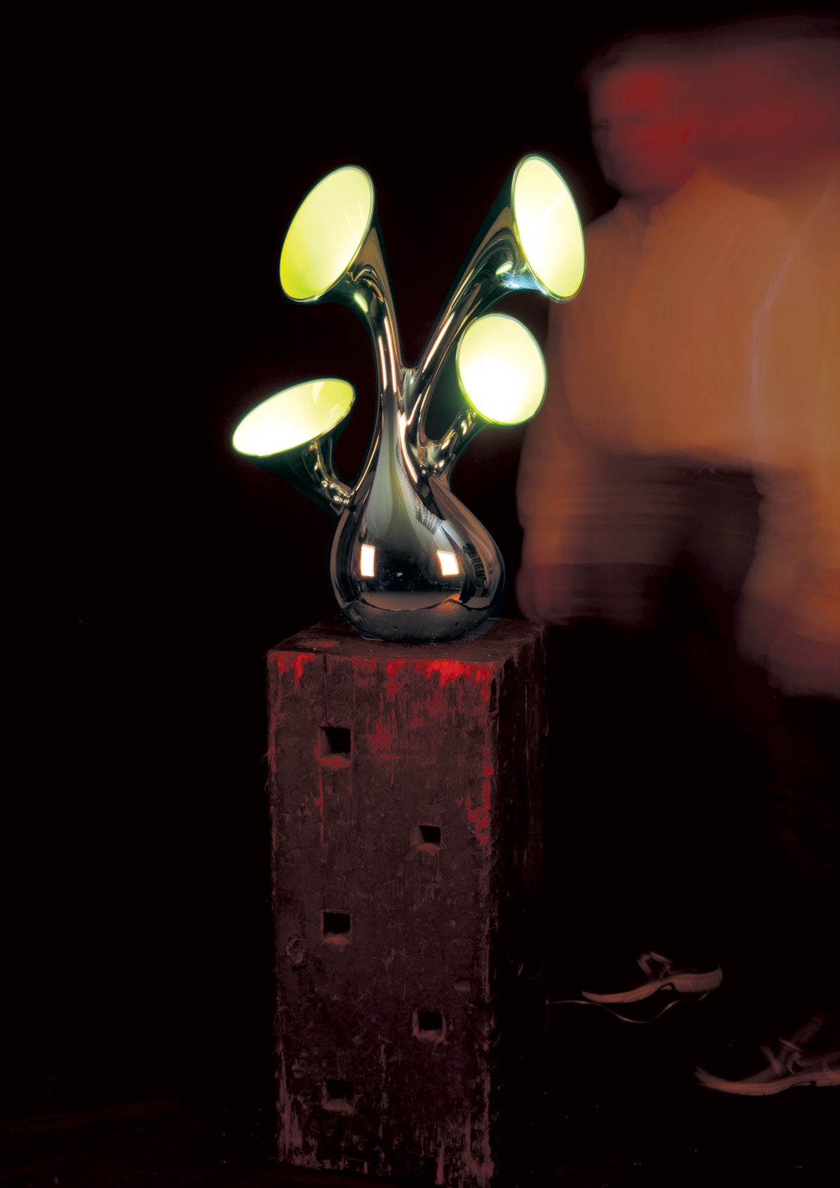 A modern chrome lamp with four glowing, horn-shaped shades on a rustic wooden block.