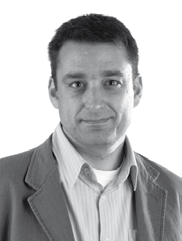 Black and white headshot of a man with short hair, wearing a striped shirt and a casual jacket, looking forward.