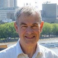 Headshot of a smiling man with grey hair against a city waterfront background.