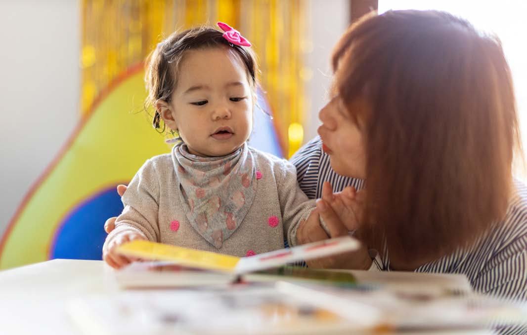 An adult and a young child look at a book together, conveying early literacy and interaction.