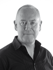 Black and white headshot of an older man with short hair, wearing a dark collared shirt, looking forward.