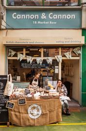 Exterior of Cannon & Cannon, a charcuterie and cheese shop, with two women behind a market stall.